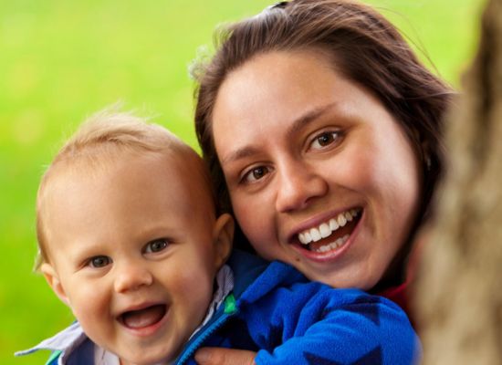 A woman holding her baby; they're both smiling at the camera