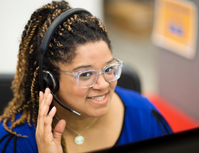 A woman in a blue shirt wearing a headset looking up towards the camera.