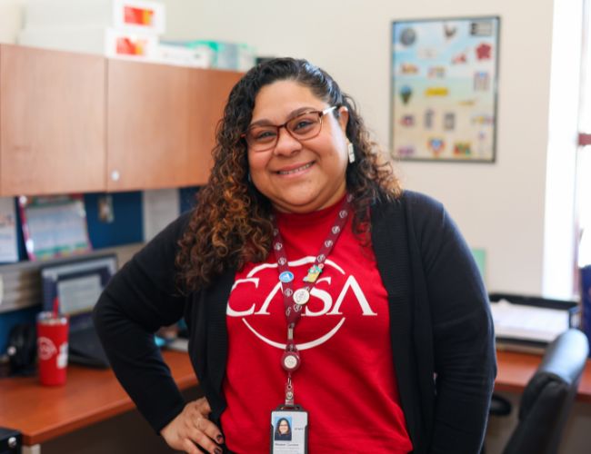 A woman wearing a red T-shirt standing in an office.