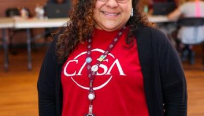 Woman with glasses smiling wearing a red CASA T-shirt.